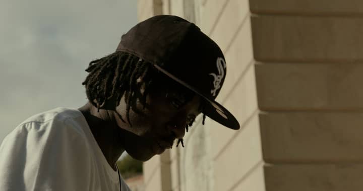 Portrait of a young African American man with dreadlocks wearing a black cap outdoors.