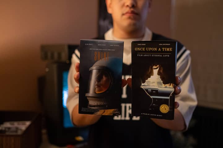 A person holding vintage VHS tapes in a cozy indoor setting.