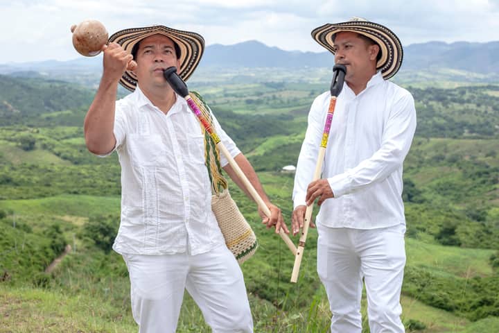 Men playing traditional flutes in the vibrant landscape of Ovejas, Colombia, showcasing cultural heritage.