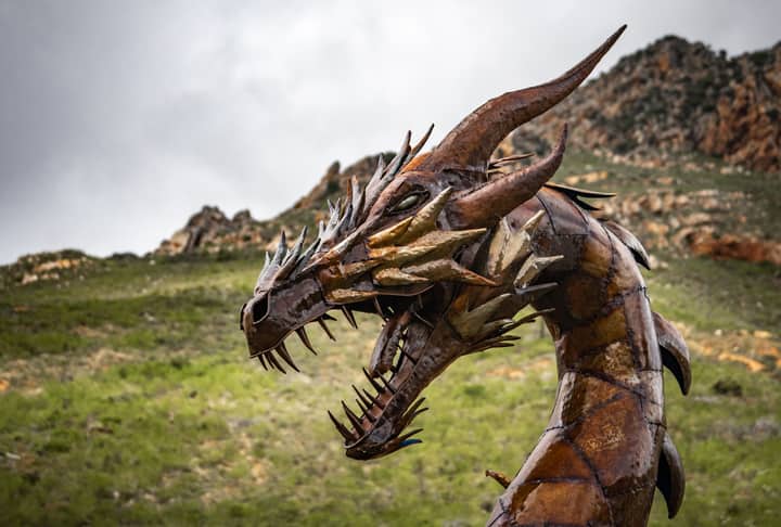 Impressive steel dragon sculpture set against a rugged and picturesque landscape.