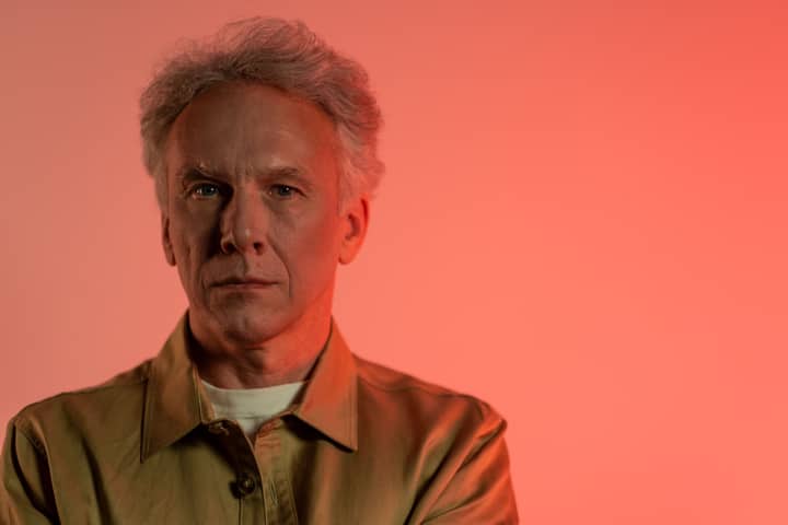Portrait of a senior man with short gray hair against a red background in a studio setting.