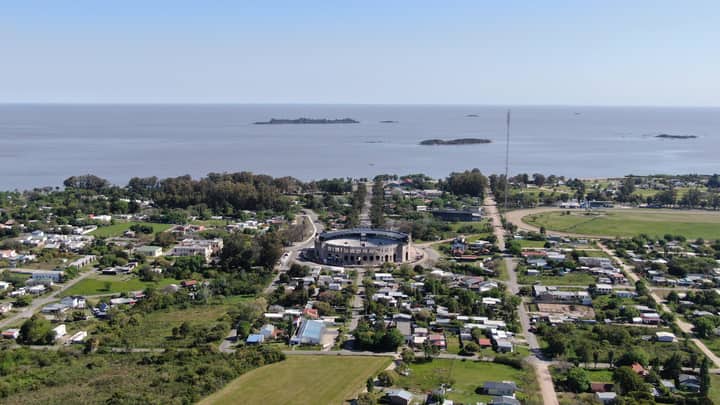Aerial view of Colonia Del Sacramento, featuring the coast and Plaza de Toros with lush greenery.