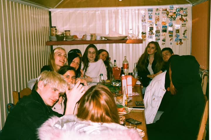 A group of young friends enjoy a casual indoor gathering at night, sharing food and drinks.