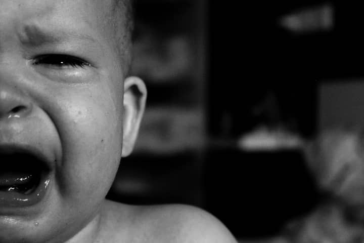 Emotional close-up of a crying baby's face captured in black and white with a blurred background.
